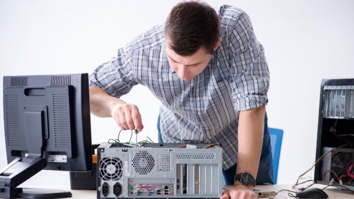 Computer technician inspecting and repairing the internal hardware of an open desktop computer.