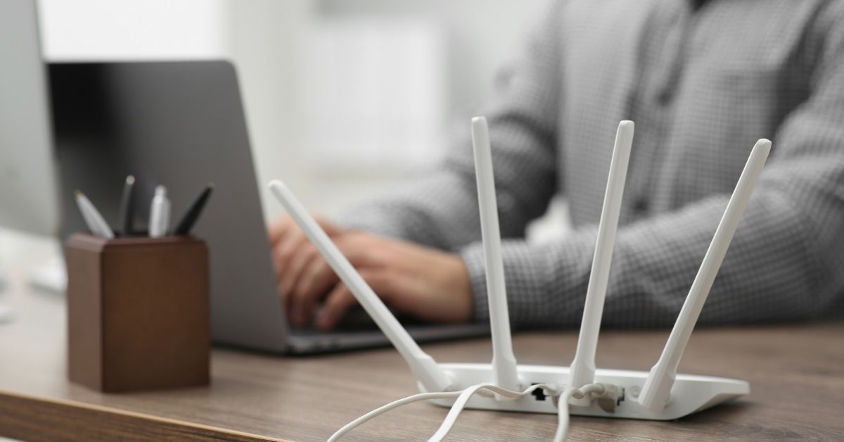 WiFi router with multiple antennas and Ethernet cables beside a laptop in a home office workspace.