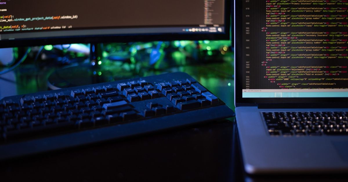 Laptop and external monitor displaying programming code in a multi-screen computer workstation setup.