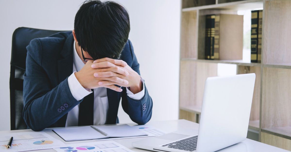 Frustrated professional sitting at a desk with a laptop and paperwork after experiencing technology problems at work.